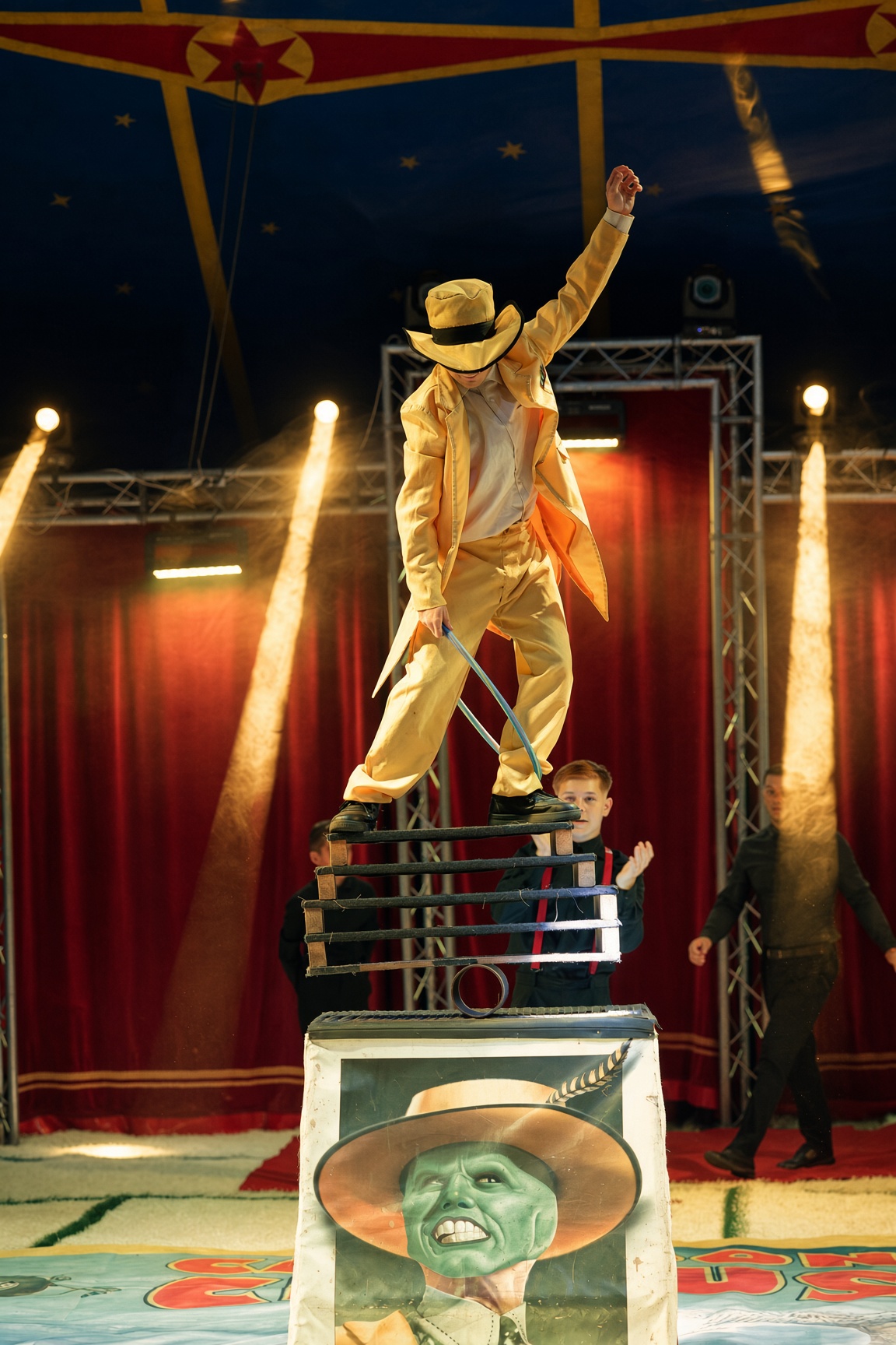 Als Maske verkleideter Artist balanciert auf Rollen und Brettern in der beleuchteten Manege