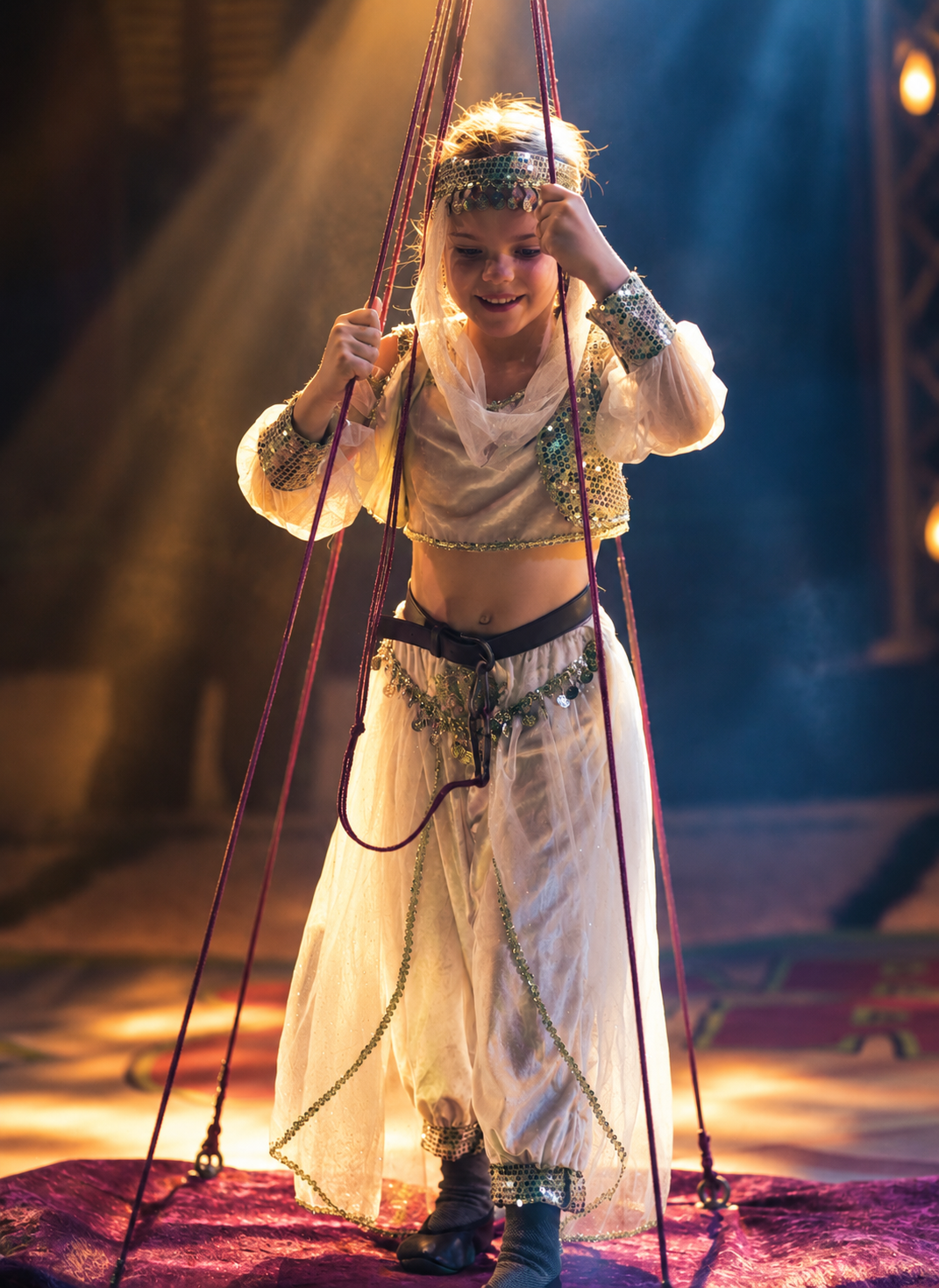 Ein junges Mädchen in orientalischem Kostüm hält sich an roten Seilen fest