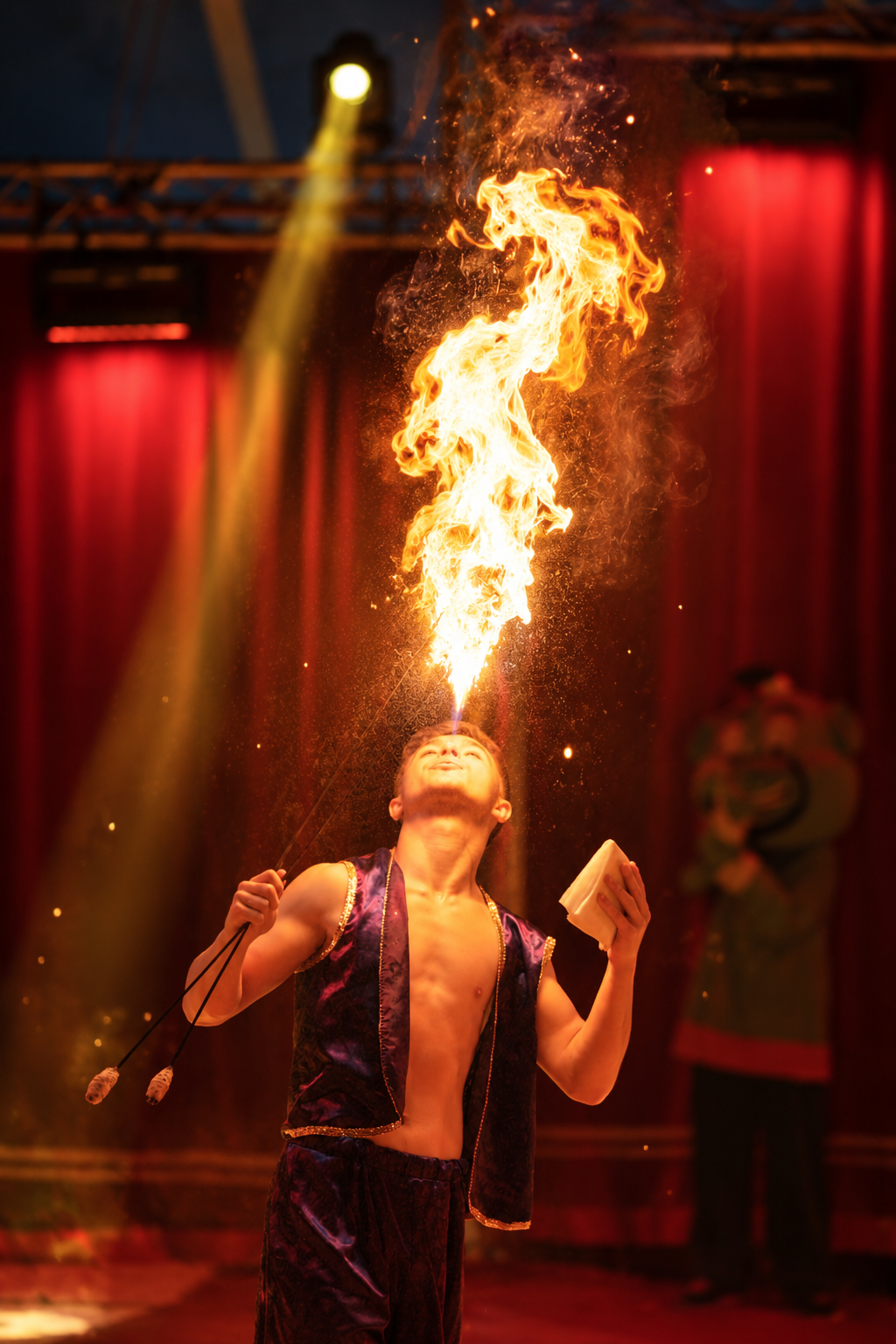 Ein Feuerschlucker speit eine große Flamme vor einem roten Zirkusvorhang